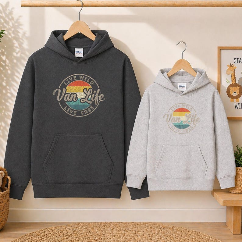 May include: Two hooded sweatshirts, one charcoal gray and one light gray, each with a front pocket and a hood. The charcoal gray sweatshirt features a circular graphic with the text "Live Wild Van Life Live Free". The light gray sweatshirt has the same graphic.