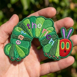 May include: An embroidered patch shaped like a green caterpillar with a red face and purple antennae. The body features various shades of green and includes the text 'eat the rich' stitched in colorful letters across the curved back segments.