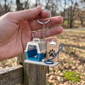 May include: A keychain featuring a blue and white pet carrier, a clipboard with a paw print and the text "Custom Name", and a stethoscope. The keychain also includes a set of keys.
