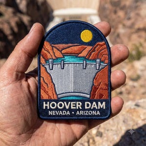 May include: A rectangular embroidered patch with rounded top corners featuring a depiction of the Hoover Dam between orange canyon walls under a dark blue sky with a yellow sun. The text reads HOOVER DAM NEVADA • ARIZONA in white lettering.