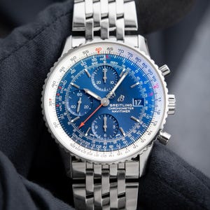 Könnte beinhalten: Eine Breitling Navitimer Chronographenuhr mit blauem Zifferblatt und silberfarbenem Edelstahlarmband. Das Zifferblatt verfügt über mehrere Hilfszifferblätter, ein Datumsfenster und eine drehbare Lünette mit Skalen. Eine Luxusuhr.