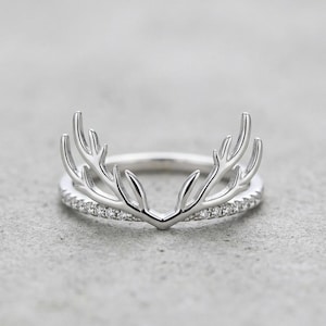 May include: A silver ring with an antler design. The ring has a band set with small, sparkling stones. The antler design sits above the band, creating a nature-inspired piece of jewellery.