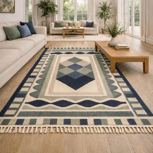 May include: A rectangular area rug with a geometric design in shades of blue, gray, and beige. The rug features diamond, wave, and rectangular patterns, with a fringed edge. The rug is placed on a hardwood floor in a living room setting.