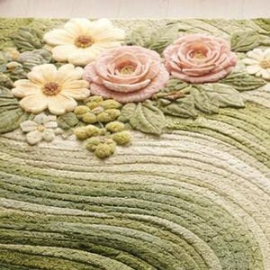 May include: A rectangular rug with a floral design. The rug features a pattern of green and cream-colored curved lines. The top of the rug has 3D flowers in shades of pink, yellow, and white, with green leaves and small green clusters.