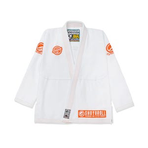Puede incluir: Kimono de Jiu-Jitsu blanco con detalles en naranja. El kimono muestra el logotipo "SHOYOROLL" en naranja en el pecho, las mangas y la parte inferior. Tiene un cuello clásico y está hecho de tela resistente.