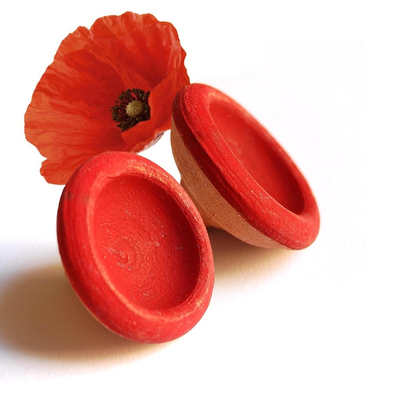 May include: Two small, red, wooden bowls with a poppy flower on a white background. The bowls are painted a vibrant red, with a natural wood color visible on the sides. The poppy is a bright red with a dark center.