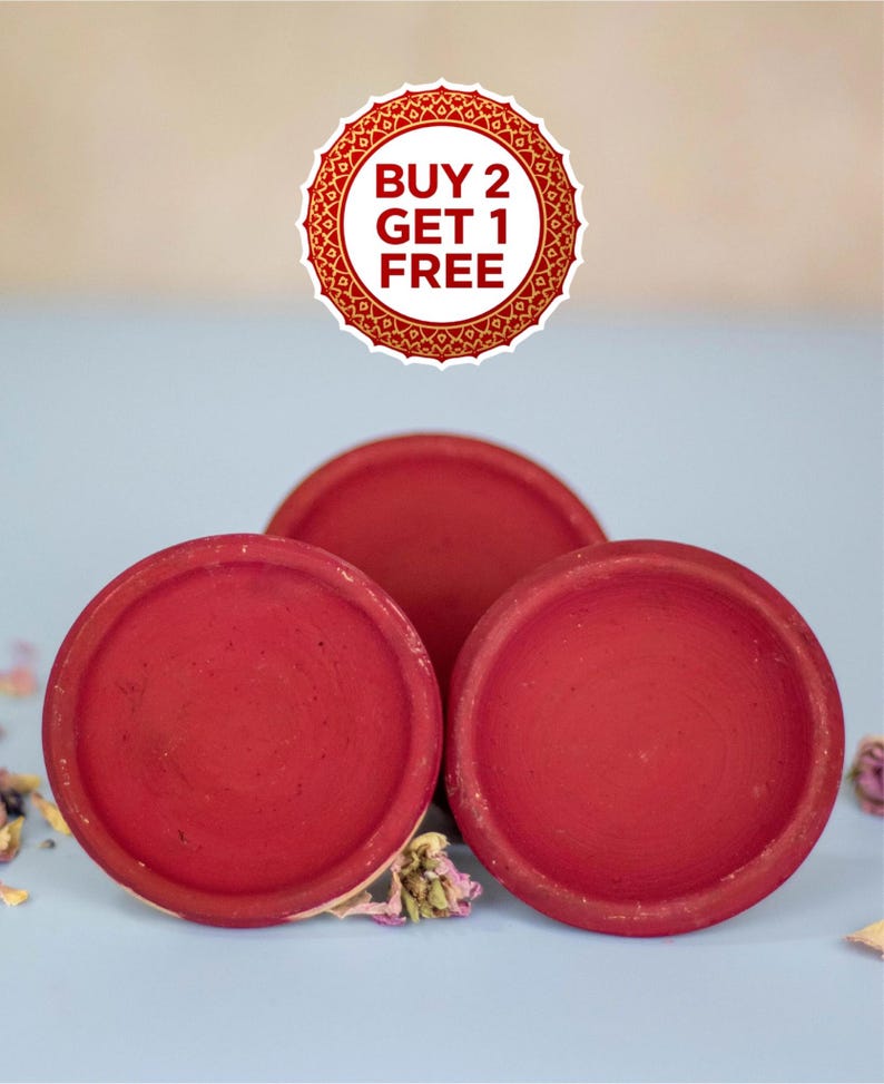 May include: Three round, red terracotta dishes are arranged on a light blue surface. The dishes have a slightly rough texture and a deep red color. A circular sticker with the text "BUY 2 GET 1 FREE" is at the top.