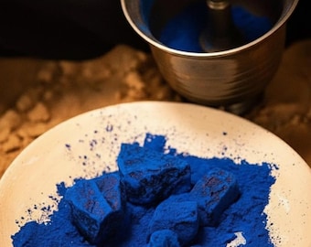 May include: A close-up shot shows a plate with vibrant blue pigment and chunks of the same color. A mortar and pestle are in use, suggesting the grinding of the pigment. The scene evokes a sense of artisanal craftsmanship and the creation of art supplies.