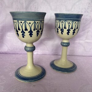 Puede incluir: Dos copas de cerámica con base crema y detalles azules. Los bordes y las bases están delineados en azul, con un patrón azul decorativo en la parte superior. Los tallos tienen un diseño bulboso.