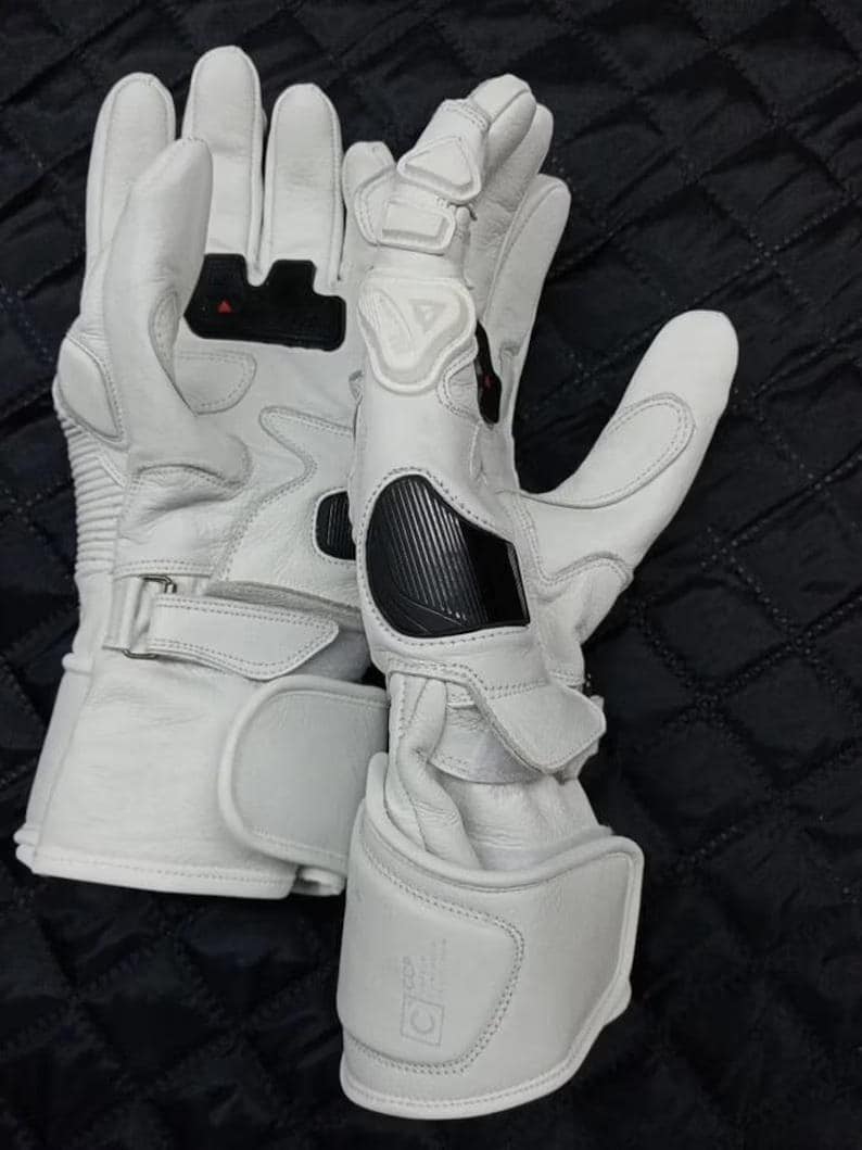May include: A pair of white motorcycle gloves with black and red accents. The gloves have reinforced knuckles and wrist straps for added protection. The design includes padded sections and a textured palm for grip. The gloves are made of leather and have a sporty aesthetic.