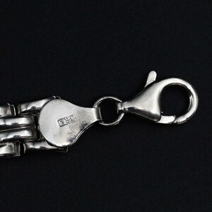 A vintage sterling silver panther style link bracelet made in Italy is displayed on a dark background, this view shows a closeup detail of the lobster clasp and the makers mark