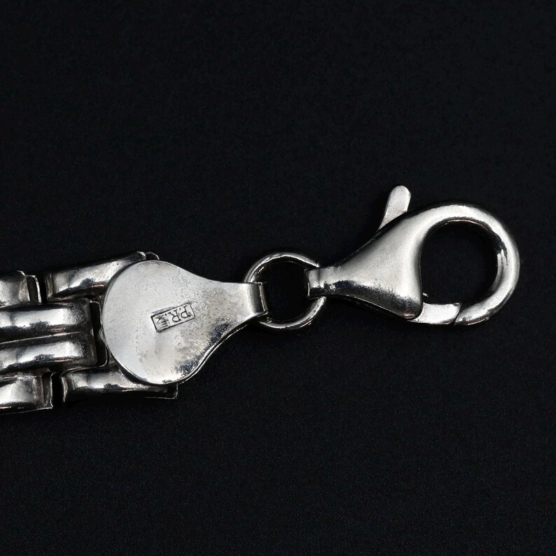 A vintage sterling silver panther style link bracelet made in Italy is displayed on a dark background, this view shows a closeup detail of the lobster clasp and the makers mark