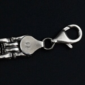 A vintage sterling silver panther style link bracelet made in Italy is displayed on a dark background this view shows the lobster clasp as well as the purity and country of origin marks