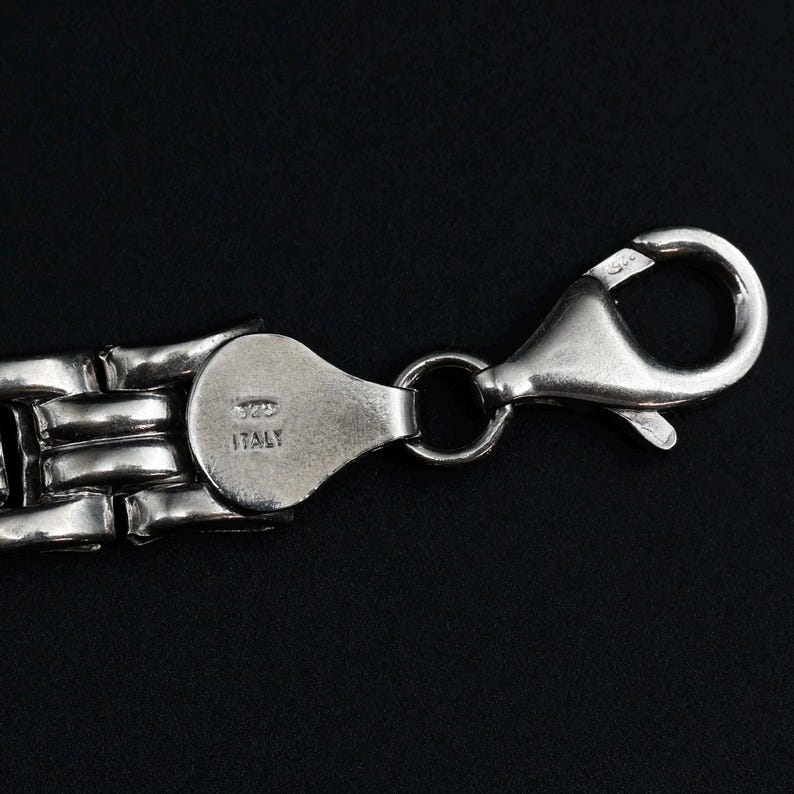 A vintage sterling silver panther style link bracelet made in Italy is displayed on a dark background this view shows the lobster clasp as well as the purity and country of origin marks