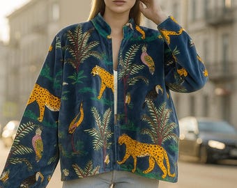 Könnte beinhalten: Dunkelblaue Jacke mit einem Dschungel-Thema-Muster mit gelben Leoparden, Tukanen und Palmen. Die Jacke hat einen Stehkragen und einen Reißverschluss vorne. Das Model trägt hellblaue Jeans.