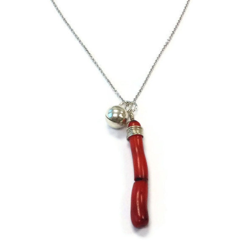 Op de afbeelding: Een zilveren ketting met een rode koraal hanger en een zilveren bel bedel.