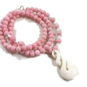 May include: A pink gemstone bead necklace with a white bone pendant in the shape of a fish hook.