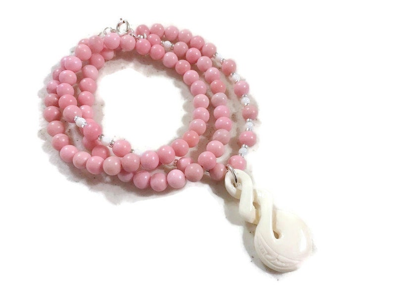 May include: A pink gemstone bead necklace with a white bone pendant in the shape of a fish hook.