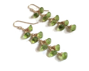 May include: Gold earrings with a cascade of green peridot gemstones. The earrings are made with wire wrapped peridot stones.