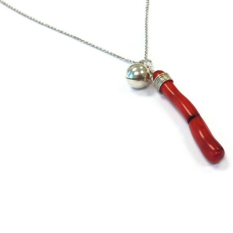 Op de afbeelding: Een zilveren ketting met een zilveren belhanger en een rode koraalhanger.
