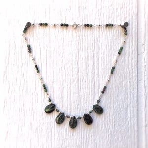 May include: A silver chain necklace with green and black gemstone beads and five teardrop-shaped green and black gemstone pendants.