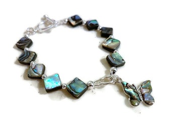 May include: A silver bracelet with a silver clasp and a silver chain attached to a silver butterfly charm. The bracelet is made of iridescent abalone shell squares.