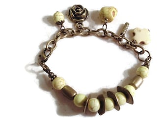 May include: A gold chain bracelet with a variety of charms, including a rose, a skull, and a star. The bracelet is adorned with light green and white beads.