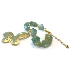 Puede incluir: Un collar de oro con un colgante de mariposa recortada y cuentas de piedras preciosas verdes.