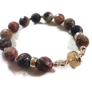 May include: A bracelet made with brown, red, and black gemstone beads and a gold clasp.