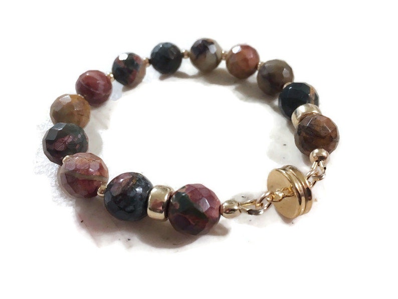 May include: A bracelet made with brown, red, and black gemstone beads and a gold clasp.