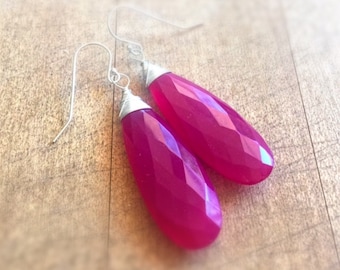 May include: A pair of dangle earrings with pink gemstone drops and silver wire wrapped around the top of each drop.