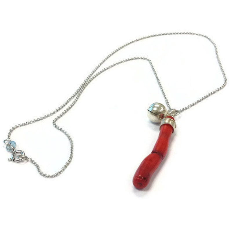Op de afbeelding: Een zilveren ketting met een rode koraal hanger en een zilveren bel bedel.