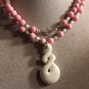 May include: A double strand necklace with pink and white beads and a carved bone pendant. The pendant is a twisted design with a hole in the center.