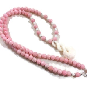 May include: A pink and white beaded necklace with a carved white bone pendant. The pendant is shaped like a knot or a swirl.