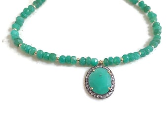 Op de afbeelding: Een ketting van groene edelstenen met een hanger met een grotere groene edelsteen omringd door kleinere diamanten.