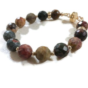 May include: A bracelet made of faceted, multi-colored gemstone beads with gold accents and a magnetic clasp.
