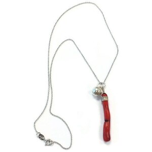 Op de afbeelding: Een zilveren ketting met een rode koraal hanger en een zilveren bel bedel.