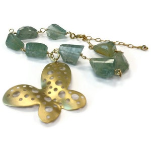 Puede incluir: Un collar de oro con un colgante de mariposa, una cadena y cuentas de piedras preciosas verdes.