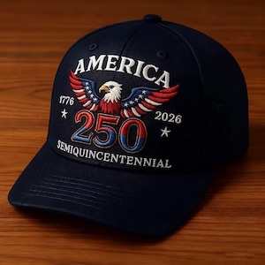 May include: A navy blue baseball cap with the word "AMERICA" embroidered in white above a patriotic eagle design. The cap features the numbers "1776" and "2026" with "250" in the center, and the word "SEMIQUINCENTENNIAL" below.