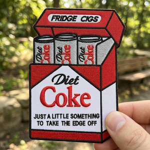 May include: Embroidered patch featuring a red and white Diet Coke box with three Diet Coke cans inside. The text "FRIDGE CIGS" is at the top, and "JUST A LITTLE SOMETHING TO TAKE THE EDGE OFF" is at the bottom.