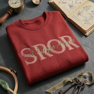 May include: A maroon sweatshirt with the embroidered text "SKappa Alpha" in a light green and beige color. The image also includes a vintage book, keys, and a brass instrument.