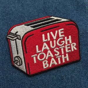 May include: Embroidered patch featuring a red toaster with silver accents and the words "LIVE LAUGH TOASTER BATH" in white. The patch is rectangular and set against a blue denim background. A fun, quirky accessory.