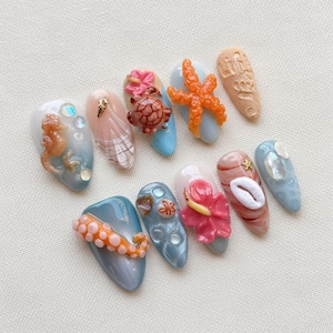 May include: A set of ten press-on nails featuring 3D ocean-themed designs including a seahorse, a turtle, a starfish, a hibiscus flower, an octopus tentacle, and seashells in shades of blue, pink, orange, and white with the text Life Good.
