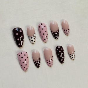 May include: A set of ten oval-shaped false nails. The nails feature various designs, including solid dark brown with white polka dots, light pink with dark brown polka dots, and nude with dark brown polka dots.