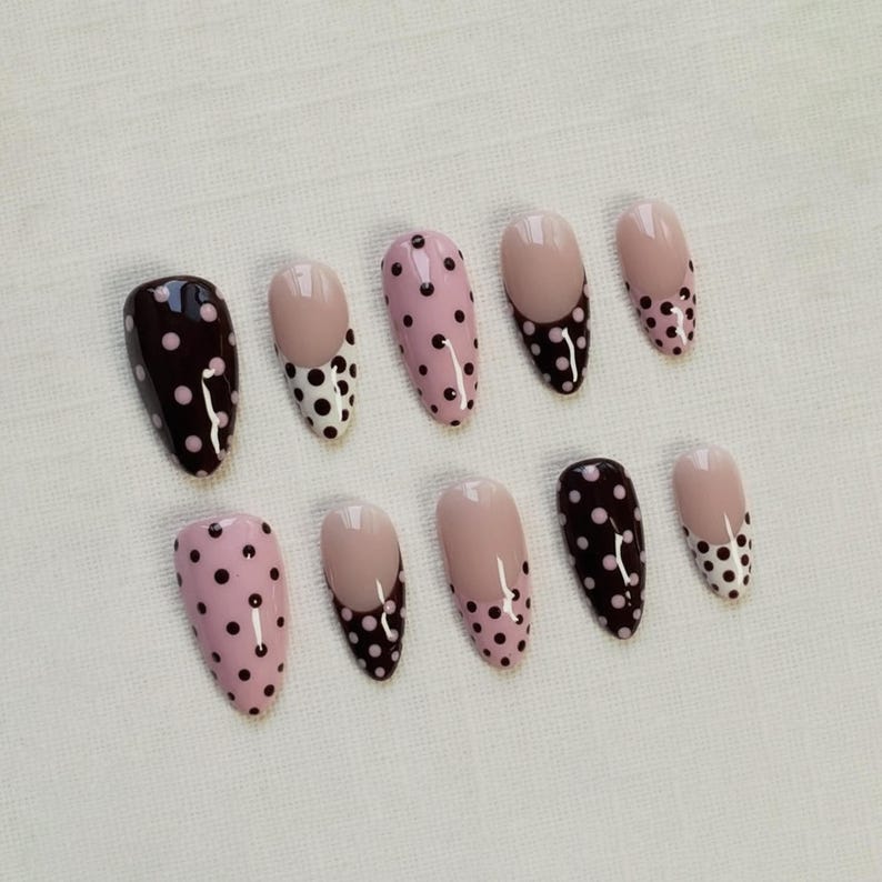 May include: A set of ten oval-shaped false nails. The nails feature various designs, including solid dark brown with white polka dots, light pink with dark brown polka dots, and nude with dark brown polka dots.