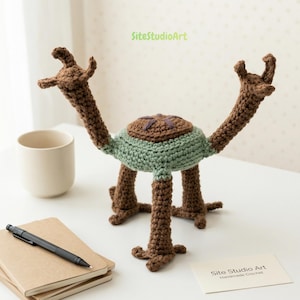 May include: A handmade crochet creature in brown and green. The creature has a round body, long legs, and two long arms. The text "SiteStudioArt Handmade Crochet" is visible on a small card.