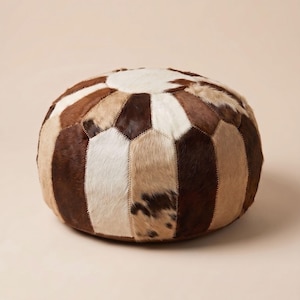 Peut inclure: Un pouf rond en patchwork dans les tons de marron, beige et blanc. Le pouf est composé de différentes formes géométriques en peau animale, créant une surface texturée et à motifs. Le design rappelle un ballon de football.