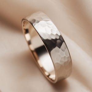 May include: A hammered metal ring with a textured surface. The ring is silver-colored and has a band with a series of small, irregular indentations. The ring is set against a soft, neutral-toned background.