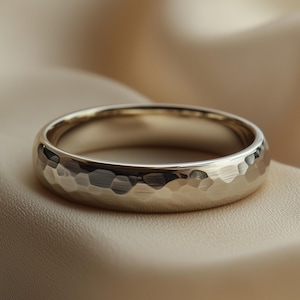 Op de afbeelding: Een goudkleurige ring met een gehamerde textuur. De ring ligt op een zachte, neutrale achtergrond. De band heeft een afgerond profiel en een getextureerd oppervlak dat licht reflecteert. Diameter ongeveer 2 cm.