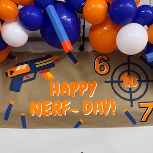 May include: A festive banner with the words "HAPPY NERF-DAY!" in orange lettering, accompanied by a toy gun illustration and a target. Balloons in orange, blue, and white are arranged above. The numbers 6 and 7 are also visible.